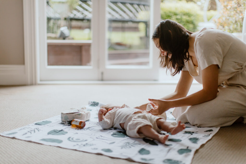 A baby and eco-friendly toys and baby items on the floorr with a mum looking down at the baby.