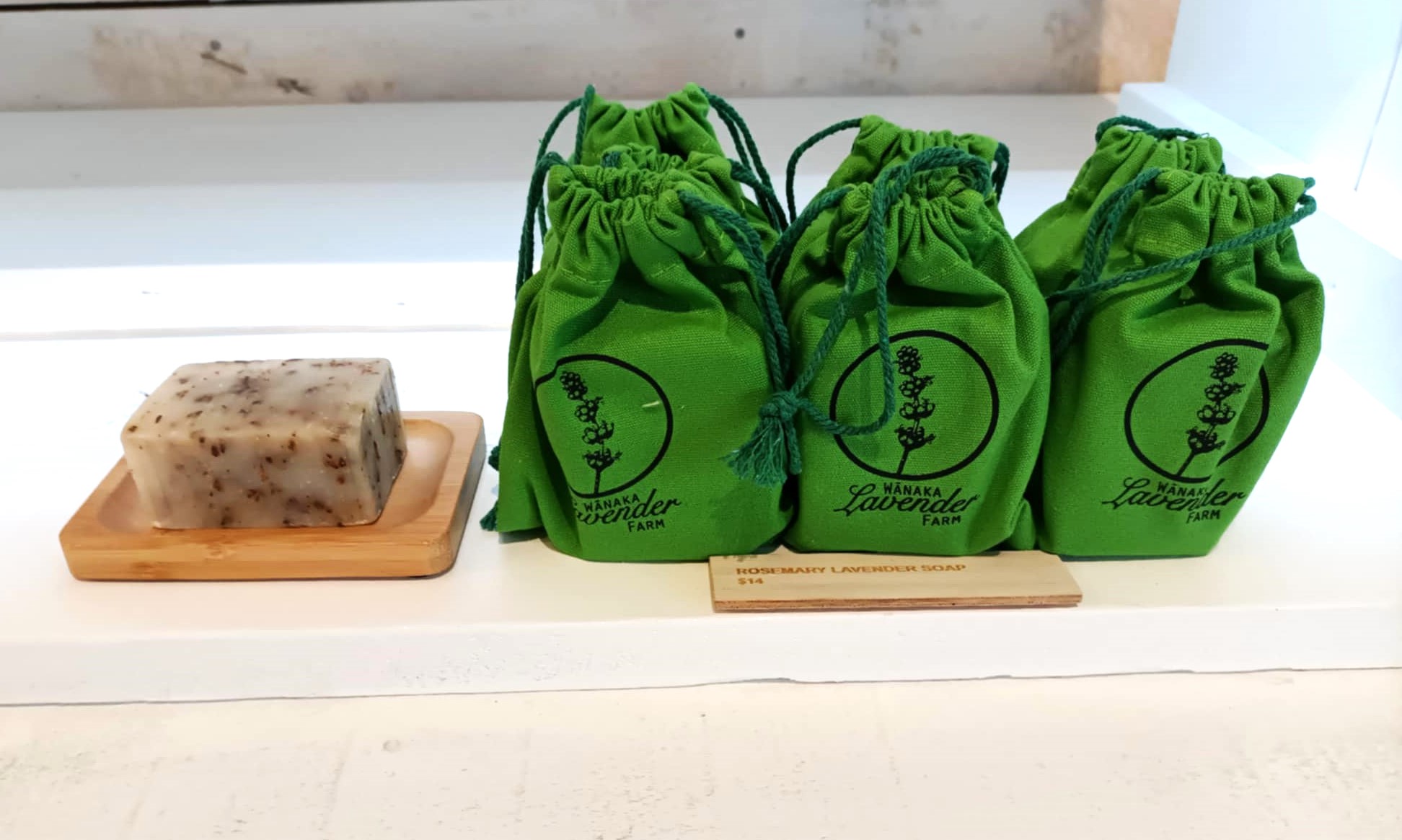 A bar of soap next to a number of bright green cotton bags from the Wānaka Lavender Farm.