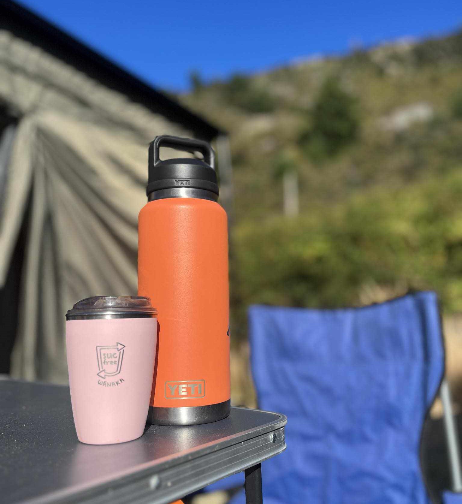 A reusable coffee cup and flask at a campsite.