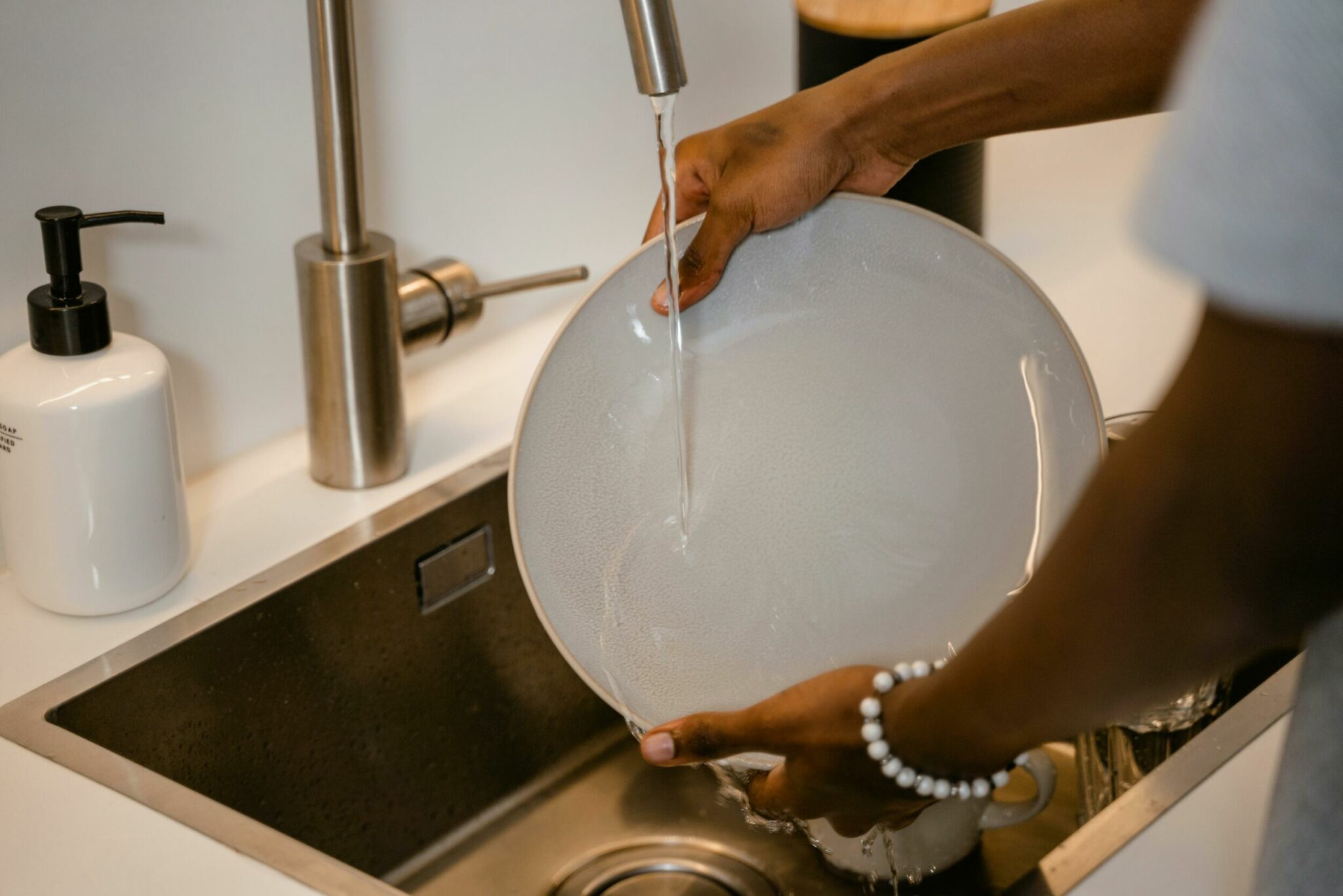 A person's hands washing dishes in a sink