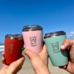 Three SUCfree cups being held together on a beach.