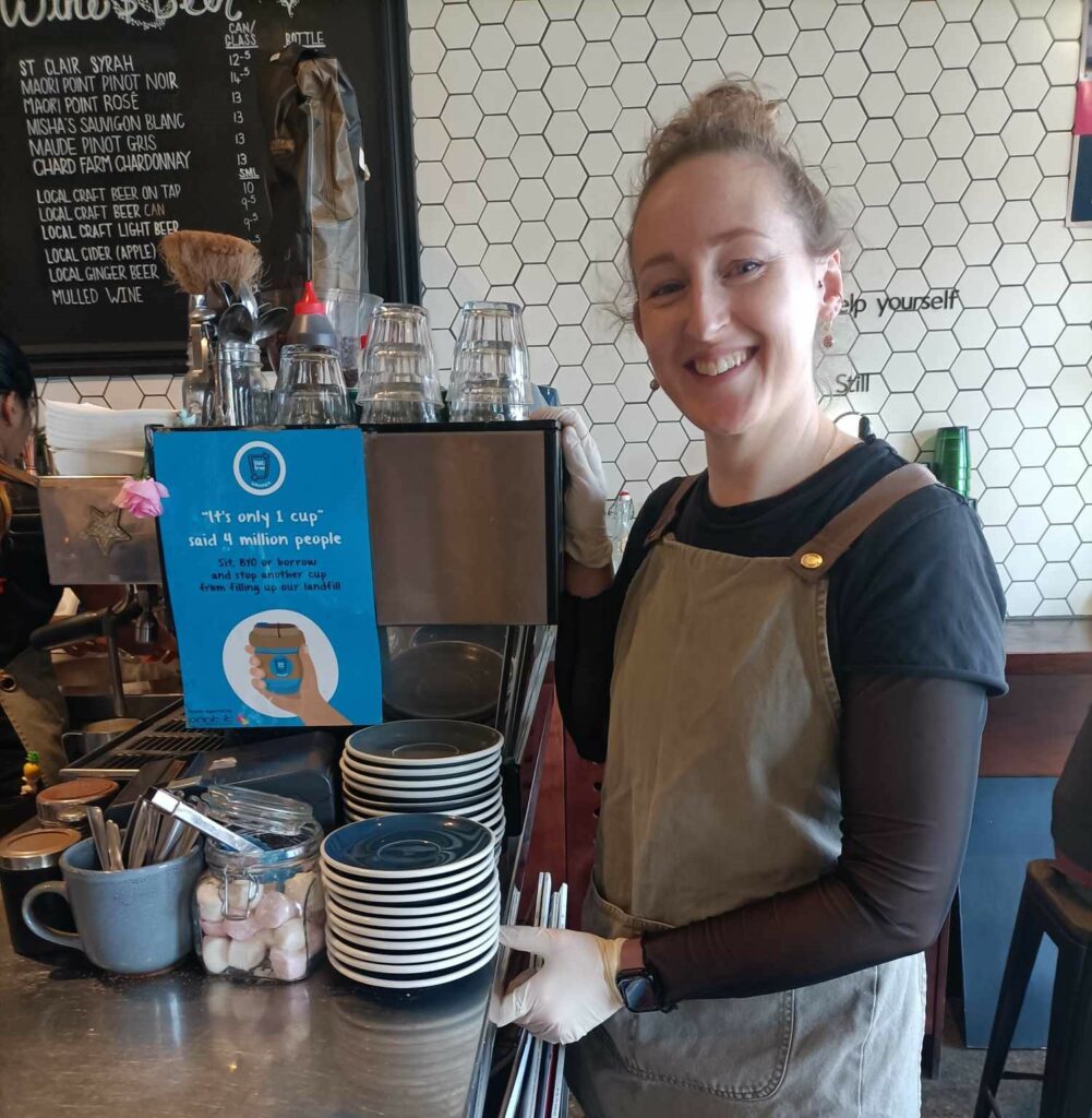A team member at Big Fig Wanaka standing next to a SUCfree poster.